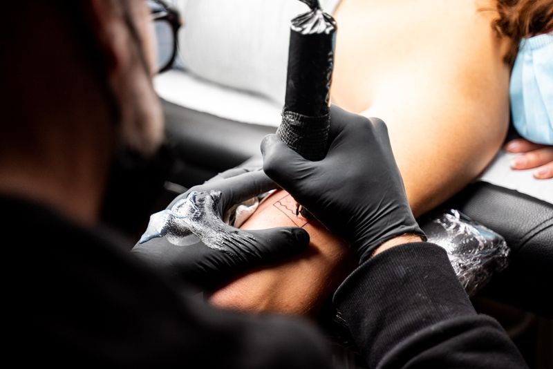 Tattoo artist applies ink to client's skin with precision in professional studio setting.