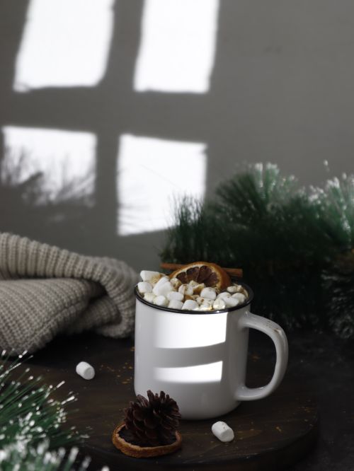 Free Warm mug of hot chocolate topped with marshmallows, surrounded by pine decor and cozy knitwear. Stock Photo