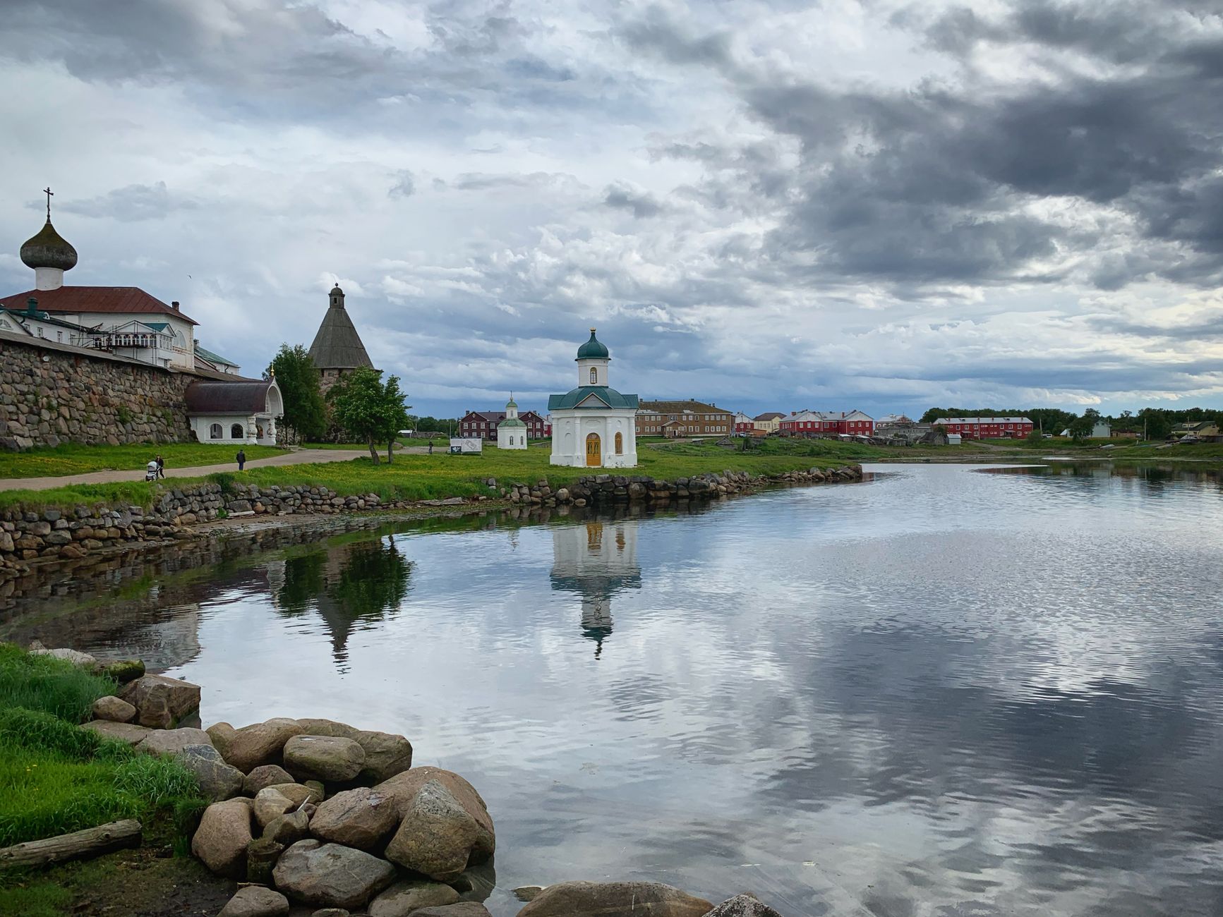 Stunning view of Solovetsky Monastery with its reflection on a calm river under cloudy skies.