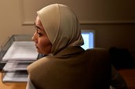 Woman in hijab working at a desk with laptop, looking over her shoulder.
