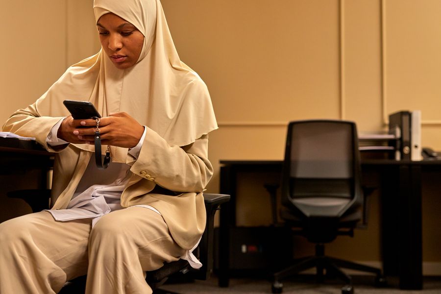 Woman in hijab reviewing content on her smartphone in an office