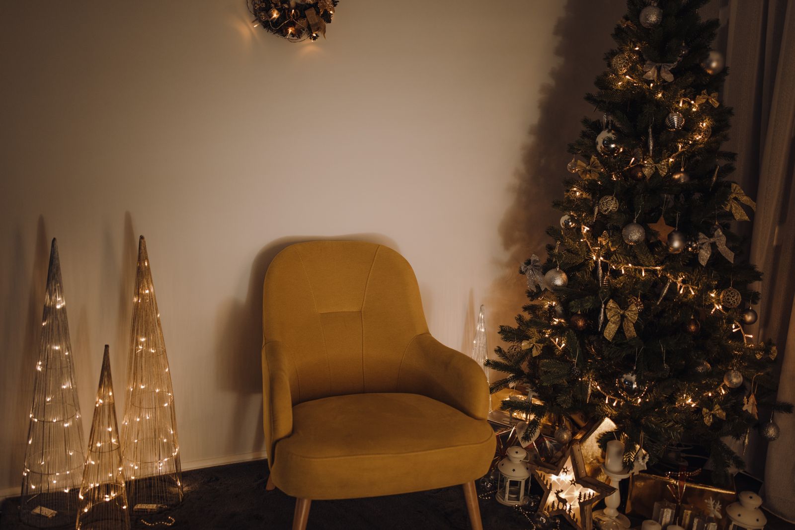 Warm lamplit sitting room with a velvet armchair, lit cone lights and a decorated evergreen — photo by Doralin Tunas on Pexels