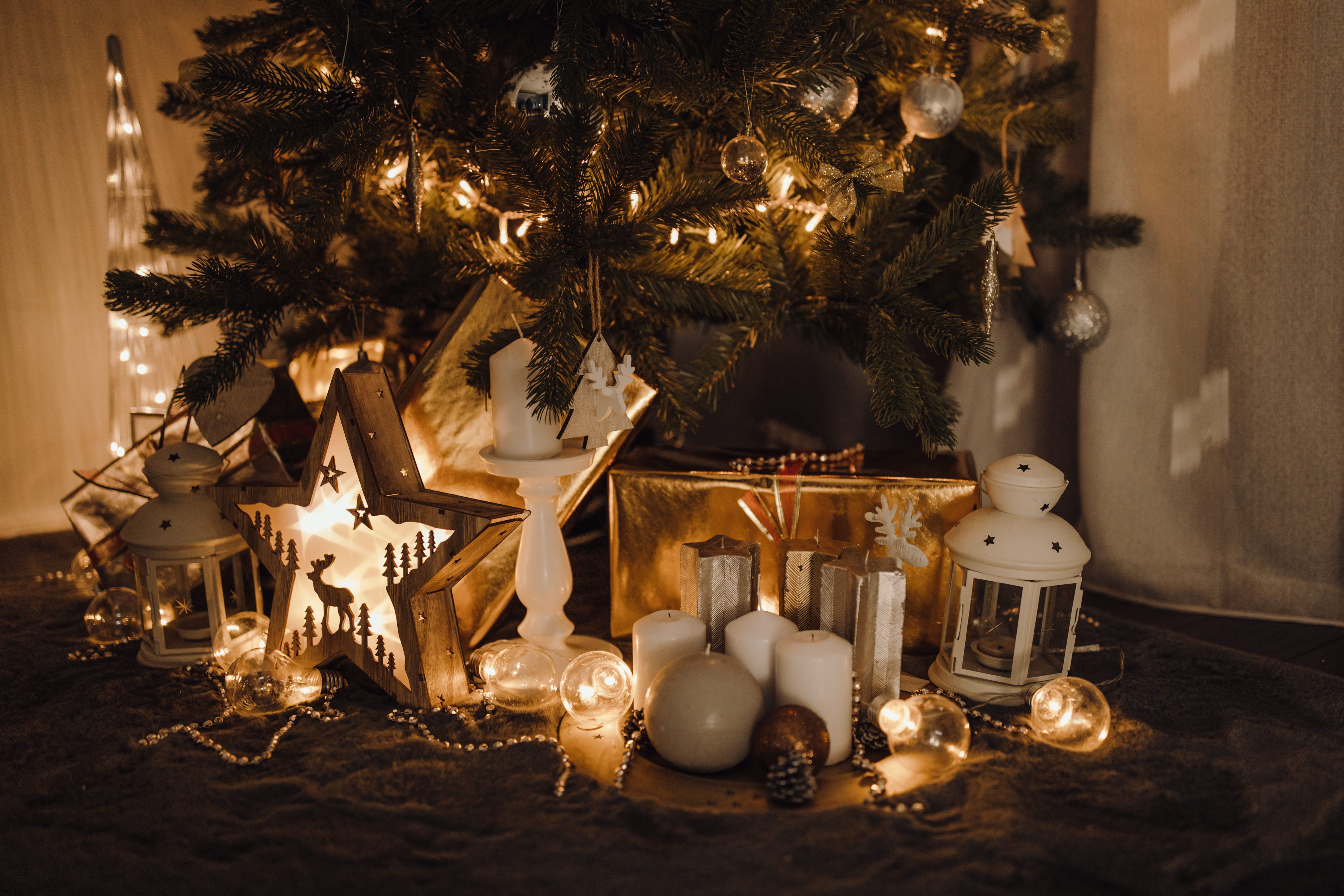 A warm and festive Christmas scene with ornaments and candles under a tree.
