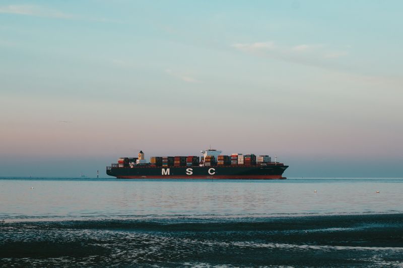 An impressive cargo ship transporting containers across a tranquil sea with a pastel sky.