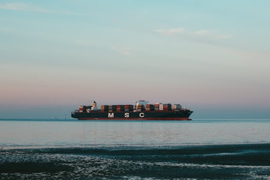 An impressive cargo ship transporting containers across a tranquil sea with a pastel sky.
