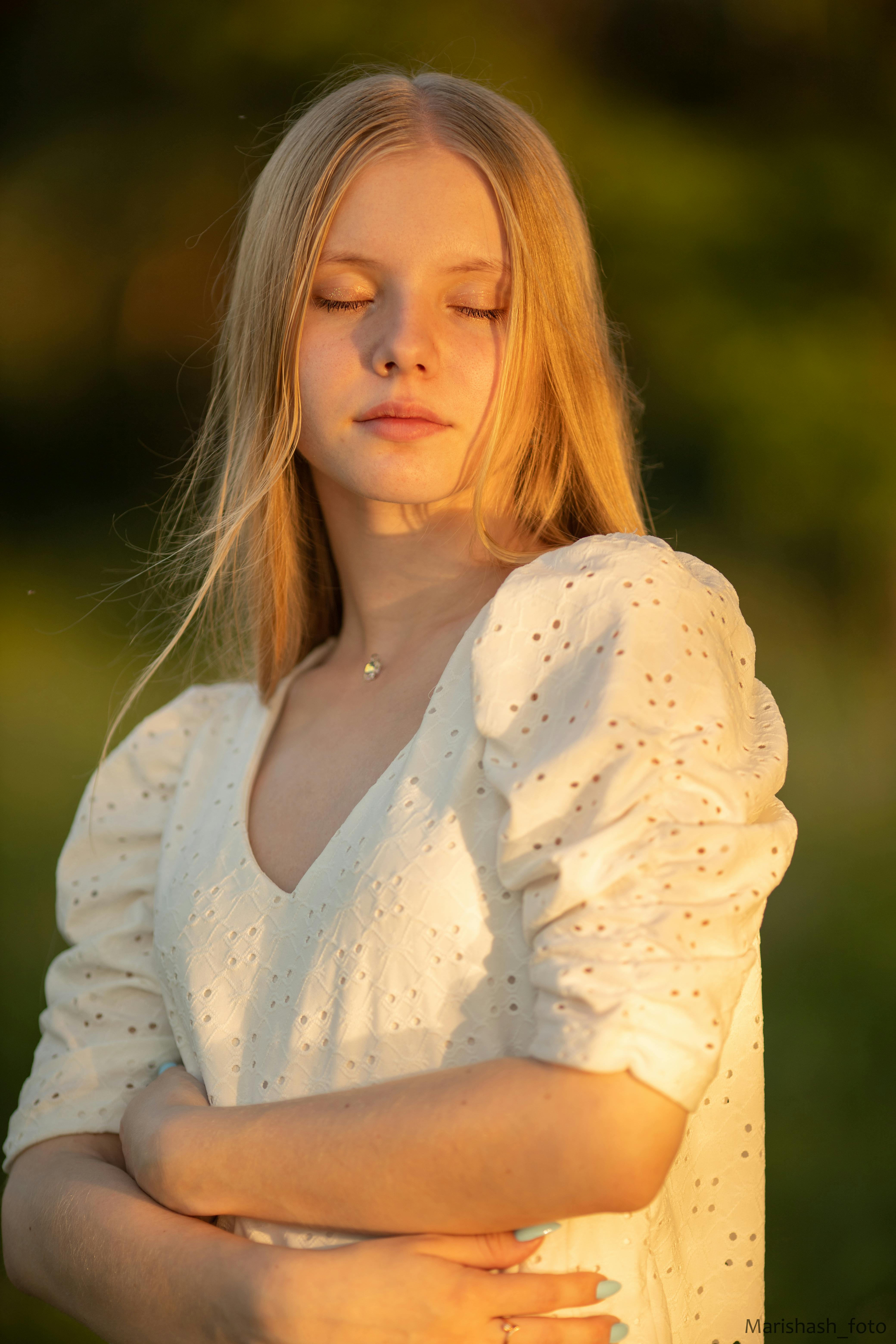 Serene portrait of a blonde woman with eyes closed, enjoying sunlight outdoors.