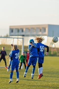 Energetic kids jumping to head a soccer ball on a sunny day on the field.