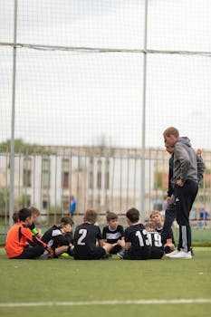 A group of young soccer players and their coach huddled on an outdoor field, focusing on teamwork and strategy.