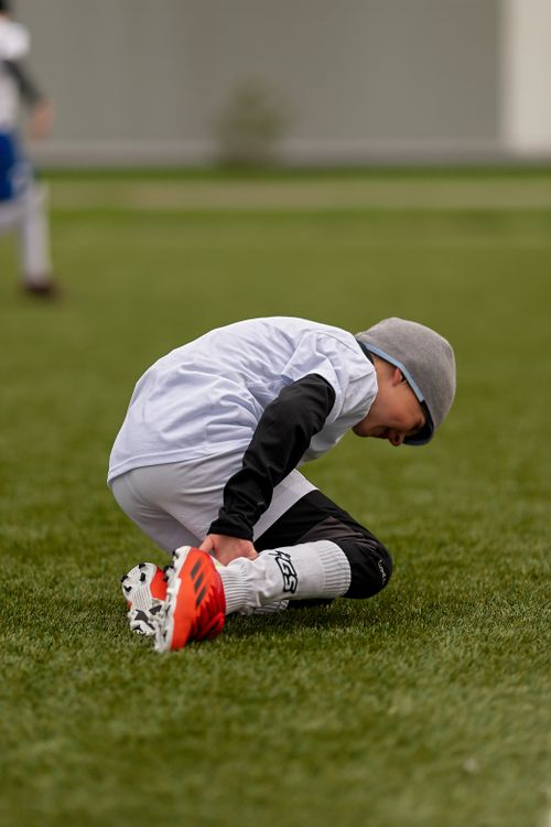 Free A young boy in sports gear kneeling on the grass during a soccer game outdoors. Stock Photo