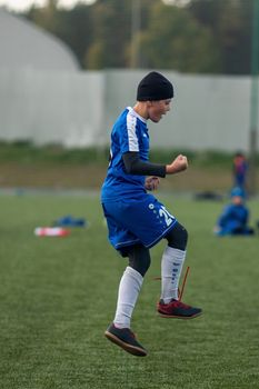 Teen soccer player in uniform joyfully jumping on the field during daytime practice.