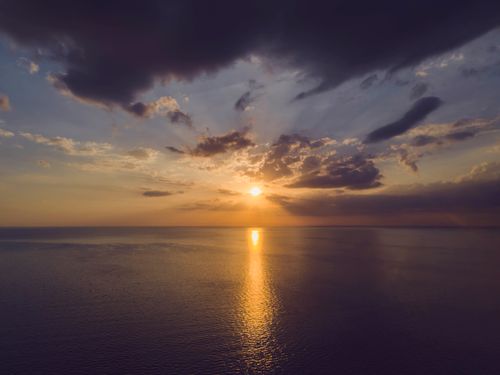 Free A tranquil ocean sunset scene with reflective waters and dramatic clouds in the sky. Stock Photo