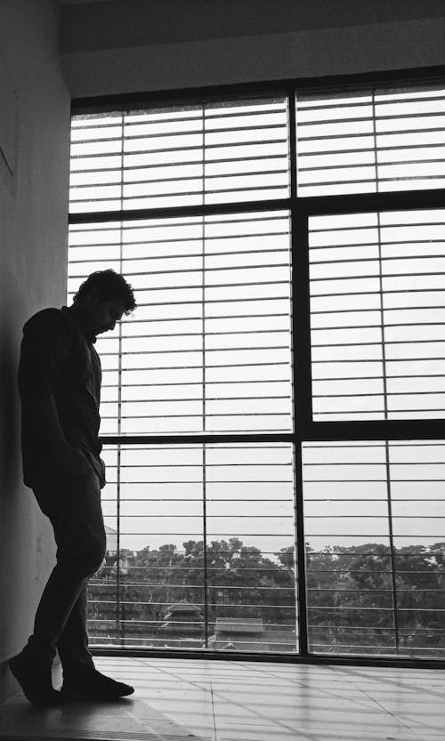 Black and White Photo of Man Standing in Front of a Wall