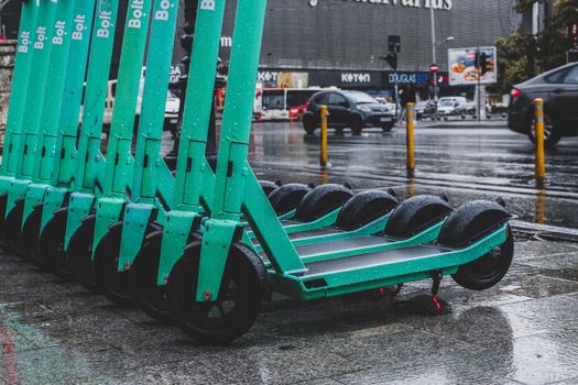 Rain-soaked electric scooters lined up on a city street, reflecting urban transportation.