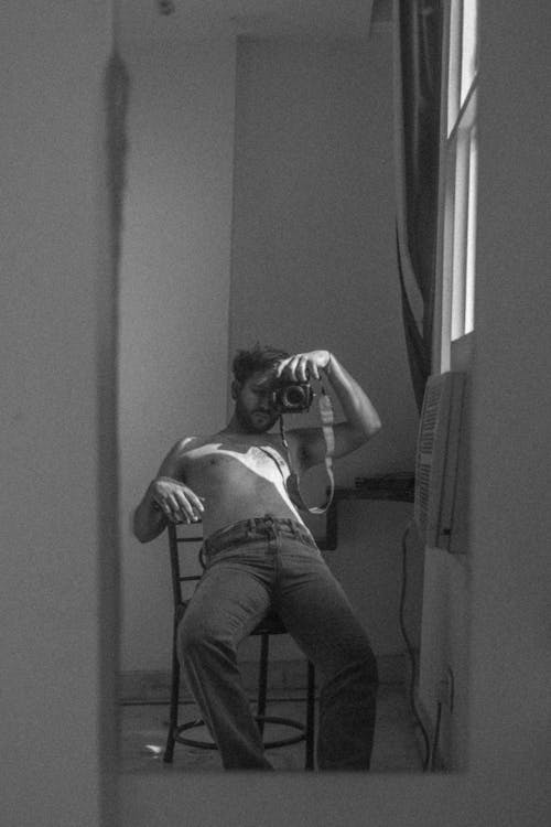 Grayscale Photo of Man Sitting on Chair While Holding a Camera