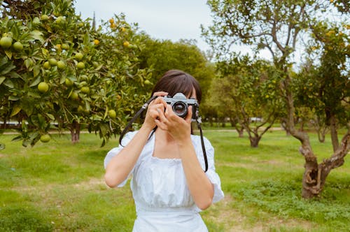 Free Woman in White Dress Holding Black Dslr Camera Stock Photo