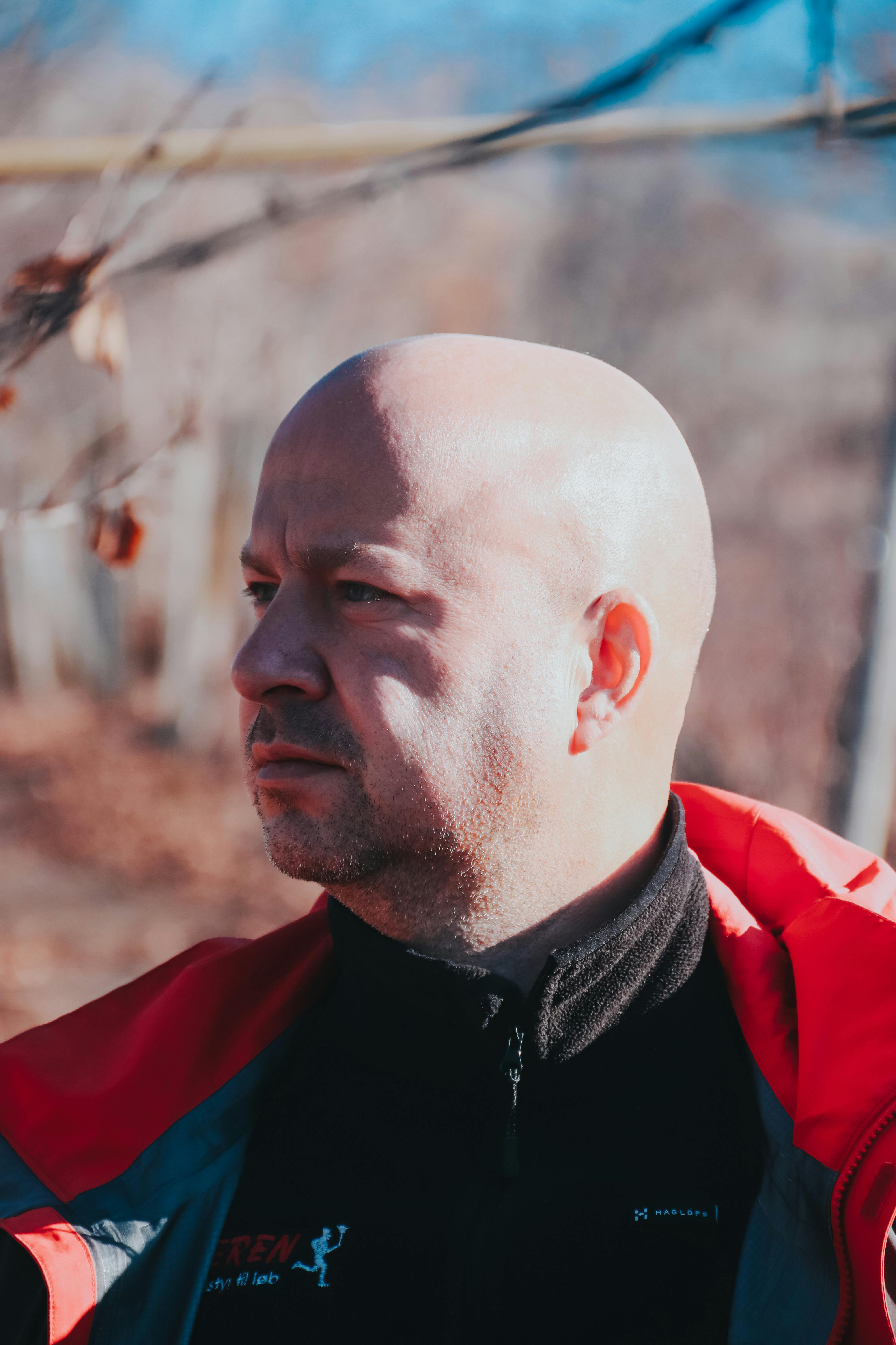 Bald man in red jacket portrait looking afar in an outdoor setting.