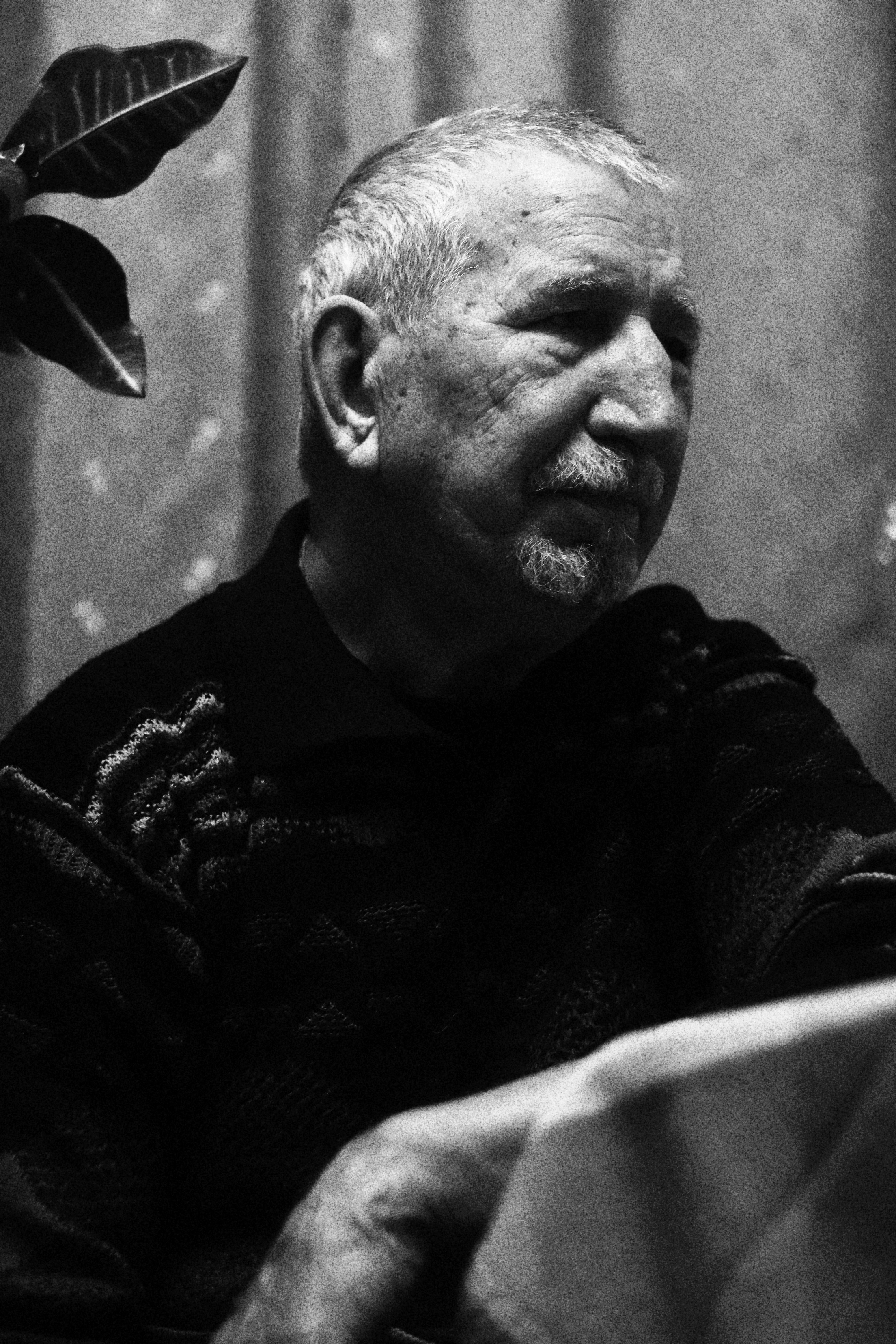 A thoughtful side profile of an elderly man in a knitted sweater, shot in black and white.