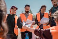 Group of volunteers in orange vests hold a community search meeting.