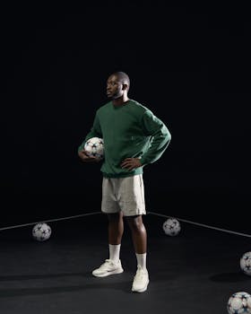 Athlete standing with soccer ball, ready for training on black background, exuding confidence.