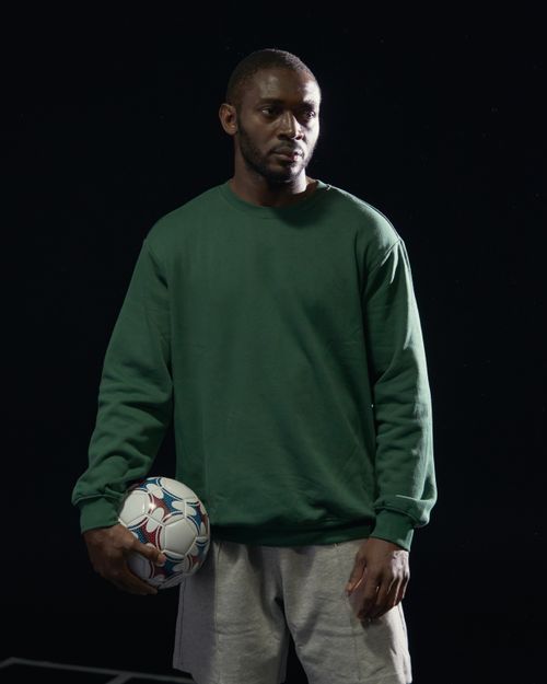 Free Studio portrait of an African American man in a green sweatshirt holding a soccer ball. Stock Photo