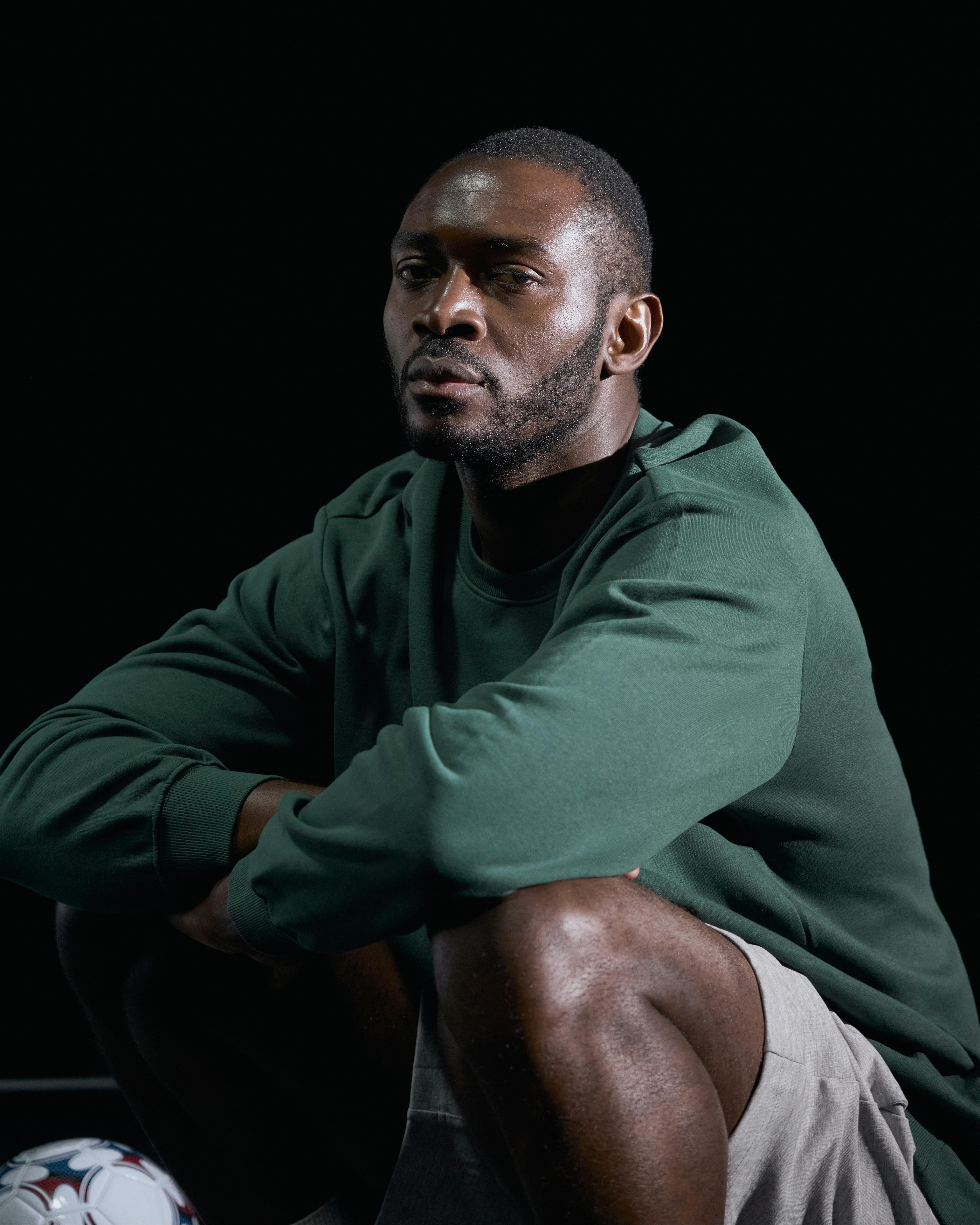 Thoughtful man in green sweater, sitting against dark background. Studio shot.