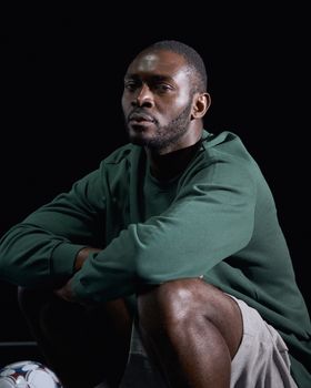 Thoughtful man in green sweater, sitting against dark background. Studio shot.