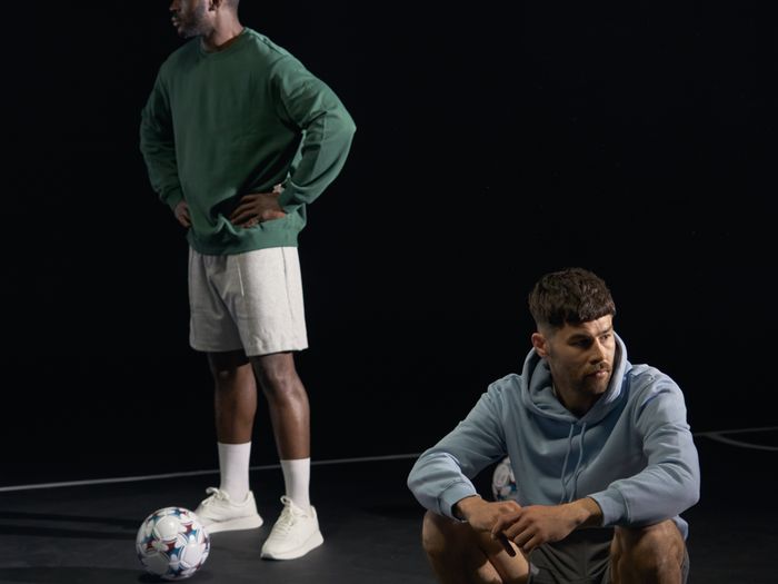 Two men in blue hoodies with footballs in a studio