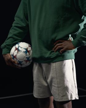 A person in sports attire holds a soccer ball in a dynamic pose on a dark background.