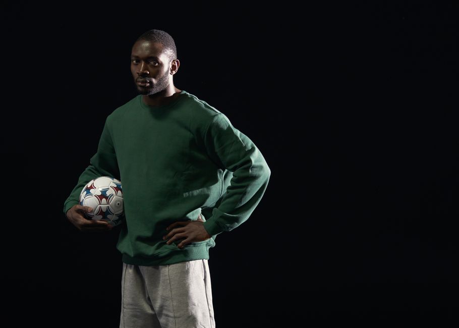 Studio portrait of a man in a green sweatshirt holding a soccer ball against a dark background.