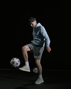 Young adult playing soccer indoors, skillfully juggling a soccer ball in a studio setting.