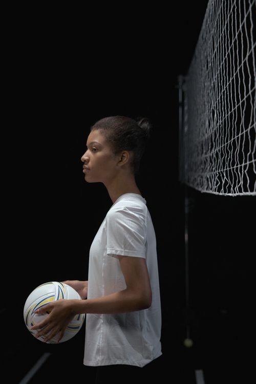 Free Young female volleyball player holding ball, standing indoors by net with determination. Stock Photo