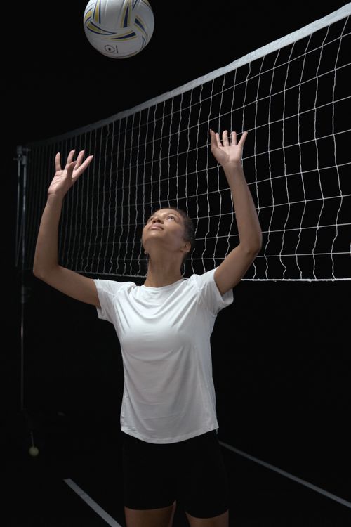 Free Athletic woman in a white shirt ready to serve a volleyball indoors. Stock Photo