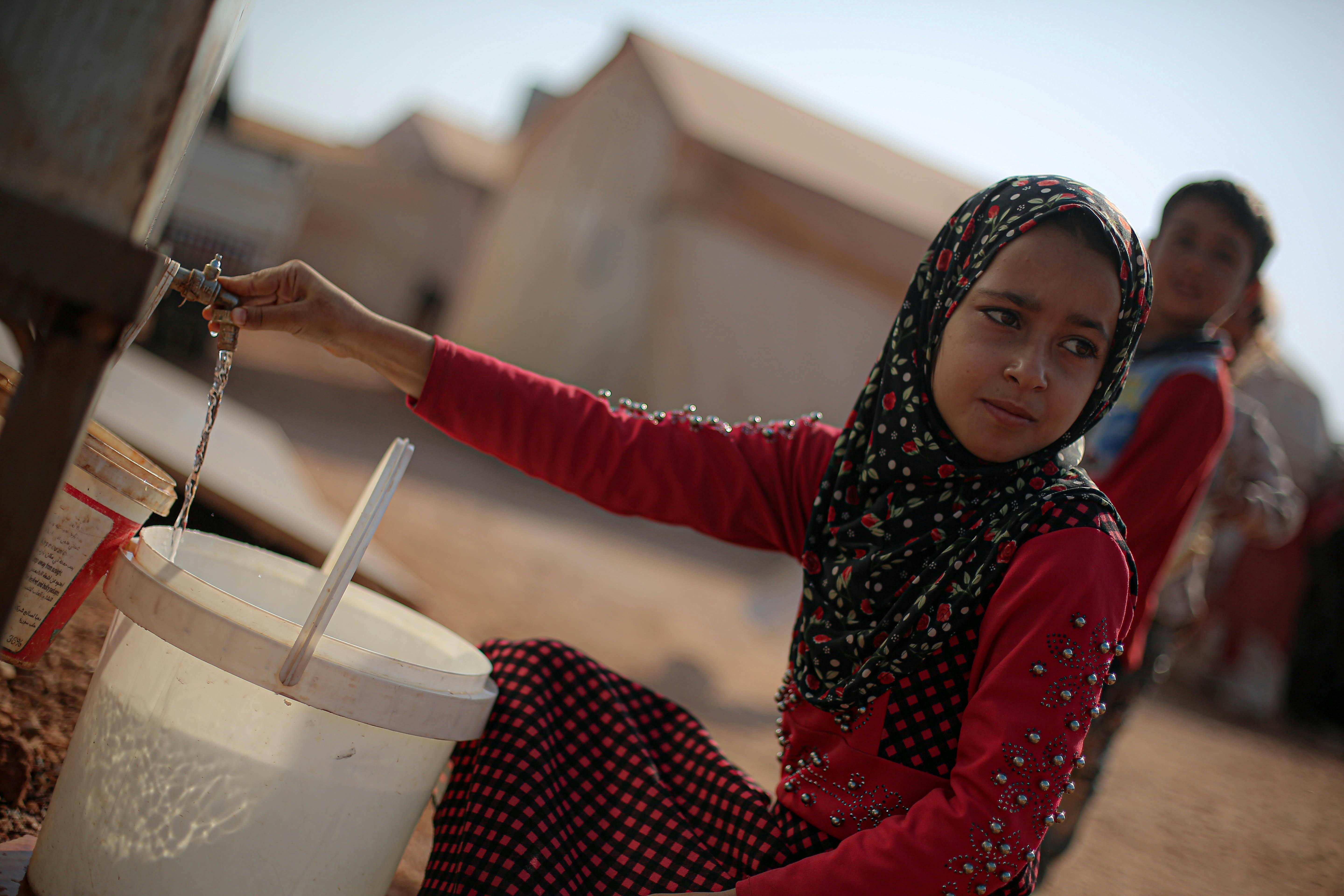 A girl in a hijab collects water at a camp in Syria. Rural life and resilience.