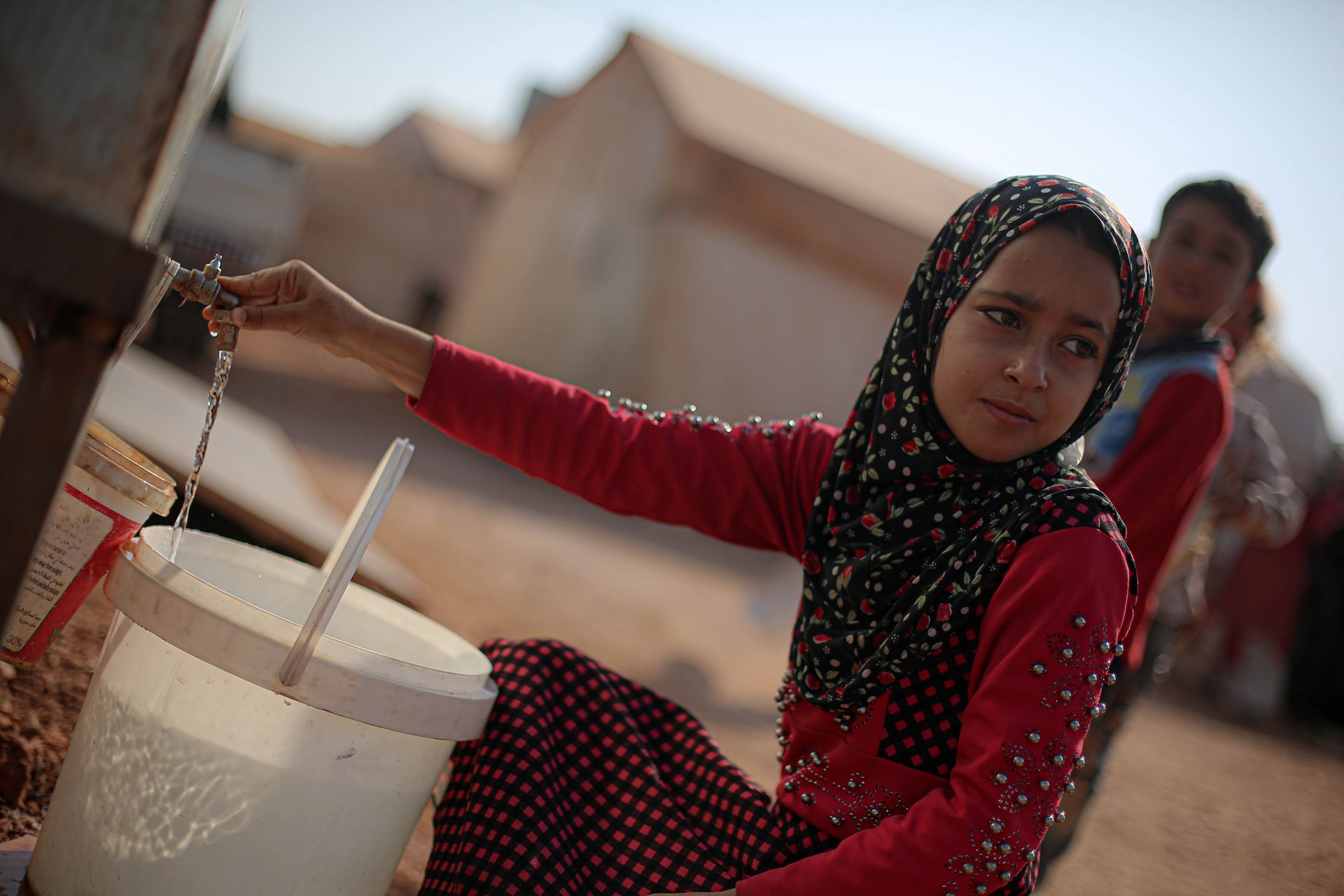 A girl in a hijab collects water at a camp in Syria. Rural life and resilience.