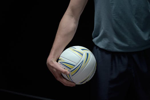 Close-up shot of a volleyball held by a person against a dark background, emphasizing sports readiness.