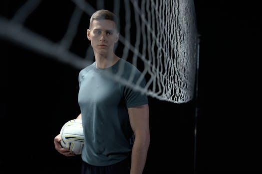 Athletic man holding a volleyball in a studio setting near a net.