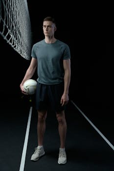 A focused young man in sportswear holding a volleyball in a dark studio setting.