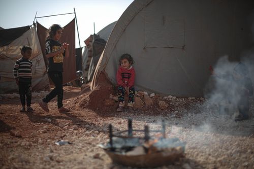 Free Children playing and resting near a tent in a Syrian refugee camp, reflecting resilience and community. Stock Photo