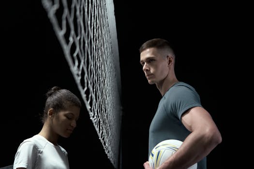 Two volleyball players face off across a net in a dramatic studio setup.
