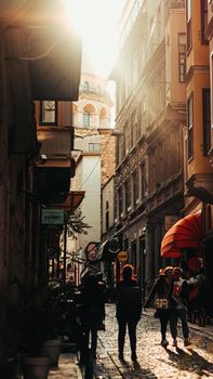 Sunlit narrow street in Istanbul with Galata Tower in view and people walking by