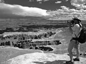 Grayscale Photo of Man Taking Photo of Canyons