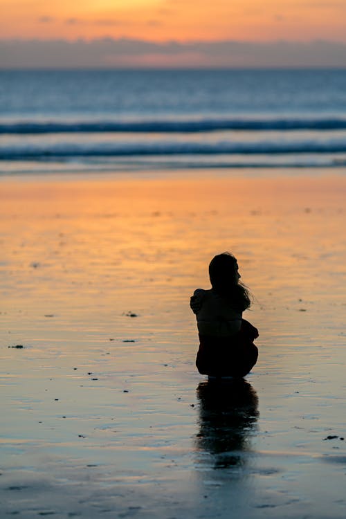 Silhouette of a Woman Sitting on the Beach during Sunset