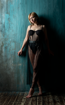 Fashion portrait of a woman posing in sheer black lingerie against a textured teal wall, showcasing elegance and style.