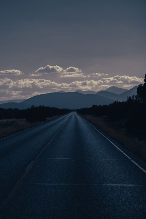 Free A calm road leading towards distant mountains under a cloudy dusk sky. Stock Photo