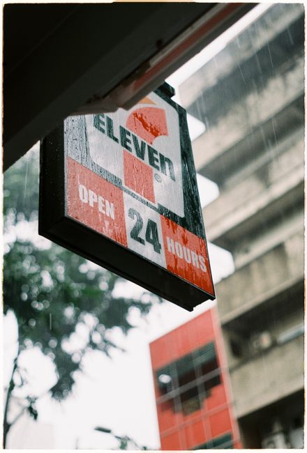 Close-up of a convenience store sign in the rain, showcasing a 24-hour service.