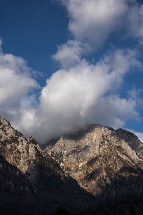 Free Dramatic mountain landscape with peaks reaching into thick clouds against a clear blue sky. Stock Photo