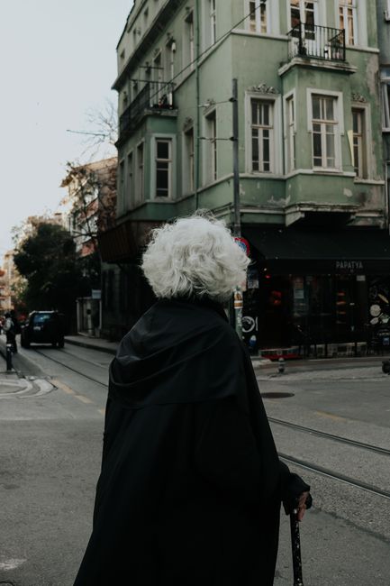 Senior woman with gray hair crossing street in urban area, showcasing city life.