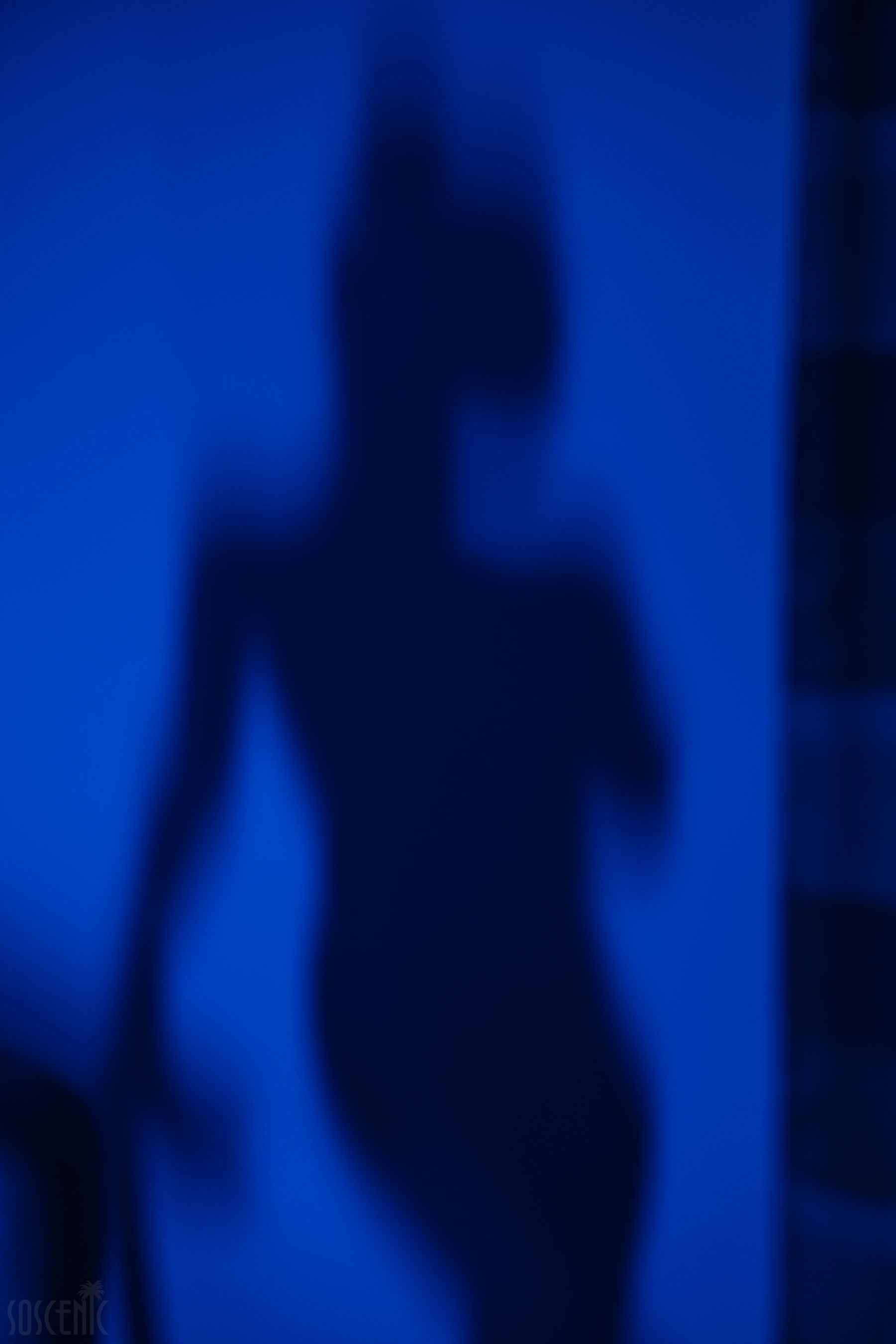 Blurry shadow silhouette on a vibrant blue wall, evoking mystery.