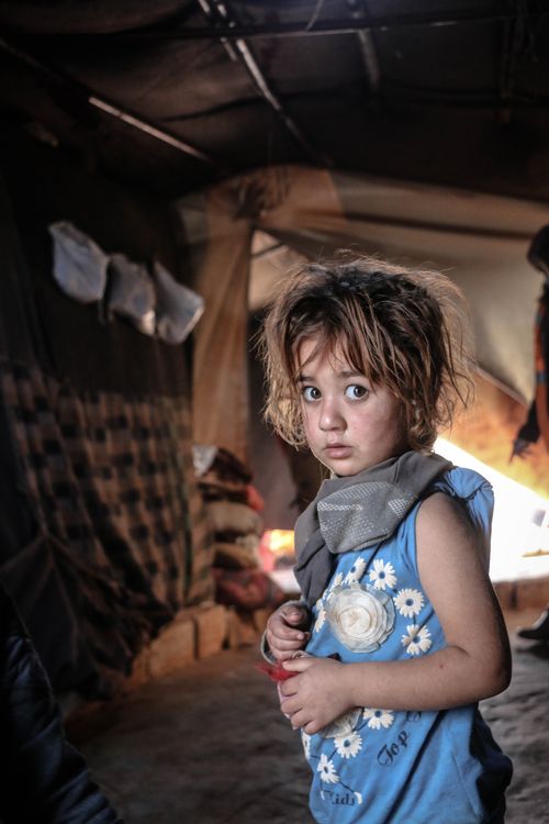 Free A young girl in a tattered dress looks on with fear inside a dimly lit shelter in Idlib, Syria. Stock Photo