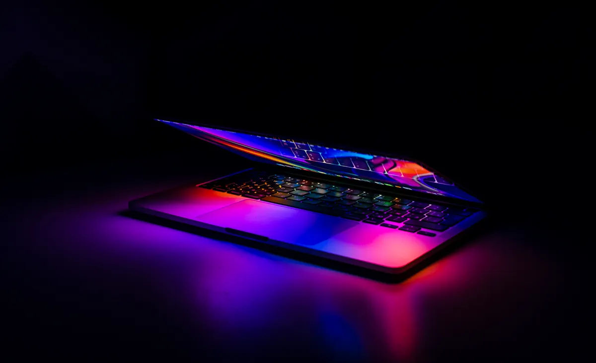 A partly open laptop glowing with blue and magenta light against a dark background, representing a trading strategy running unattended overnight.